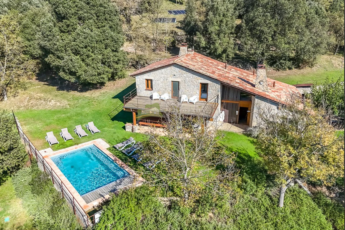 Vista aèria d'una masia de pedra amb piscina i prat, envoltada de bosc